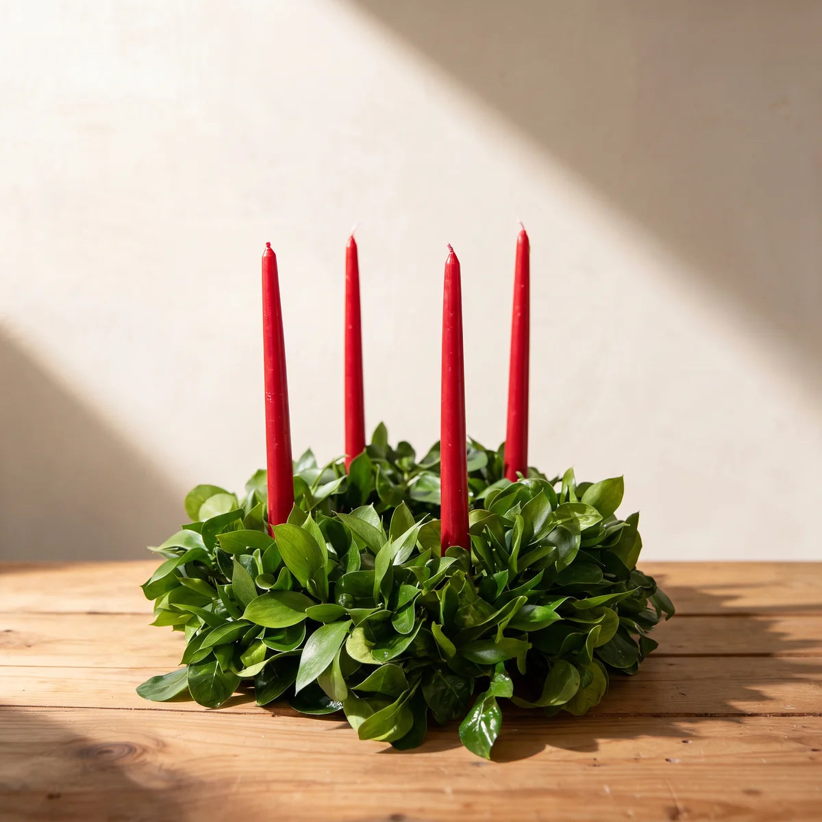 Round table wreath of fresh glossy green leaves with four red taper candles on a pine table, Fabulous Flowers South Africa