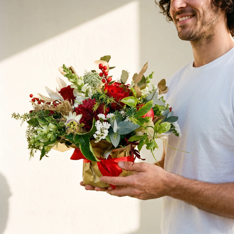 Man in a white t-shirt holding a red rose Christmas arrangement wrapped in gold paper, Fabulous Flowers South Africa