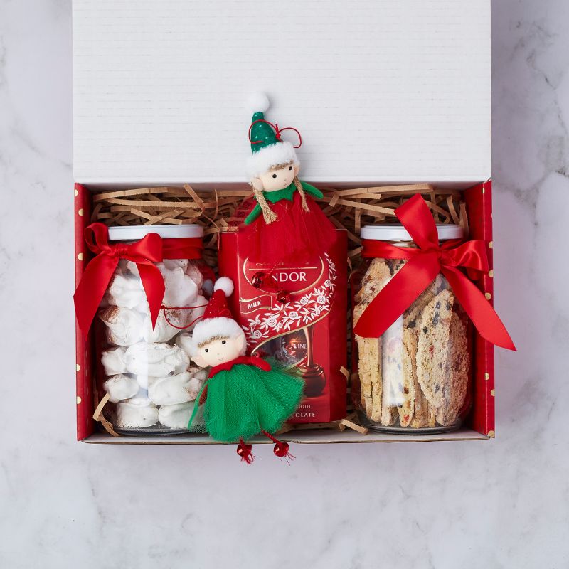 Gift box with two jars of treats, Lindor chocolate, and two festive elf dolls inside a white box with a red ribbon.