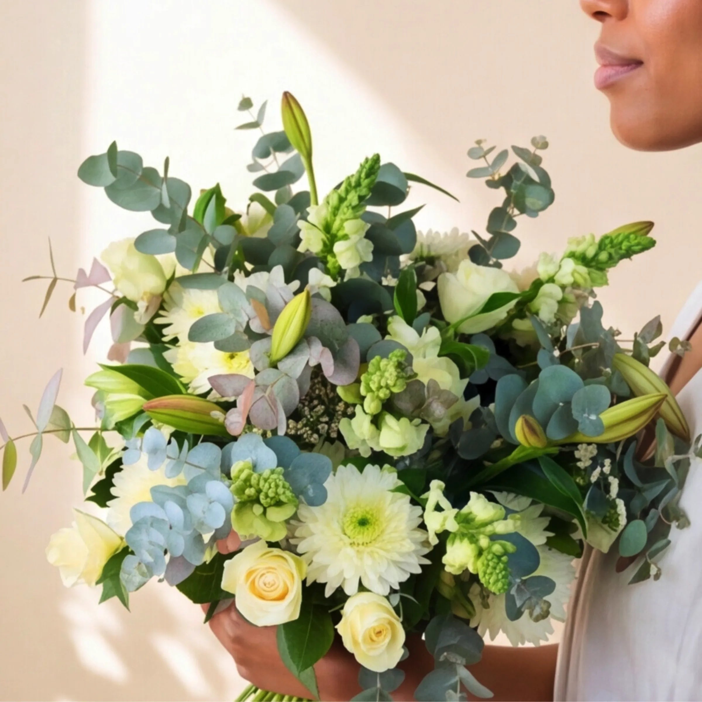 Florist holding the Classic White Bouquet ivory roses, white chrysanthemums and pale blue hydrangea hand-tied bouquet