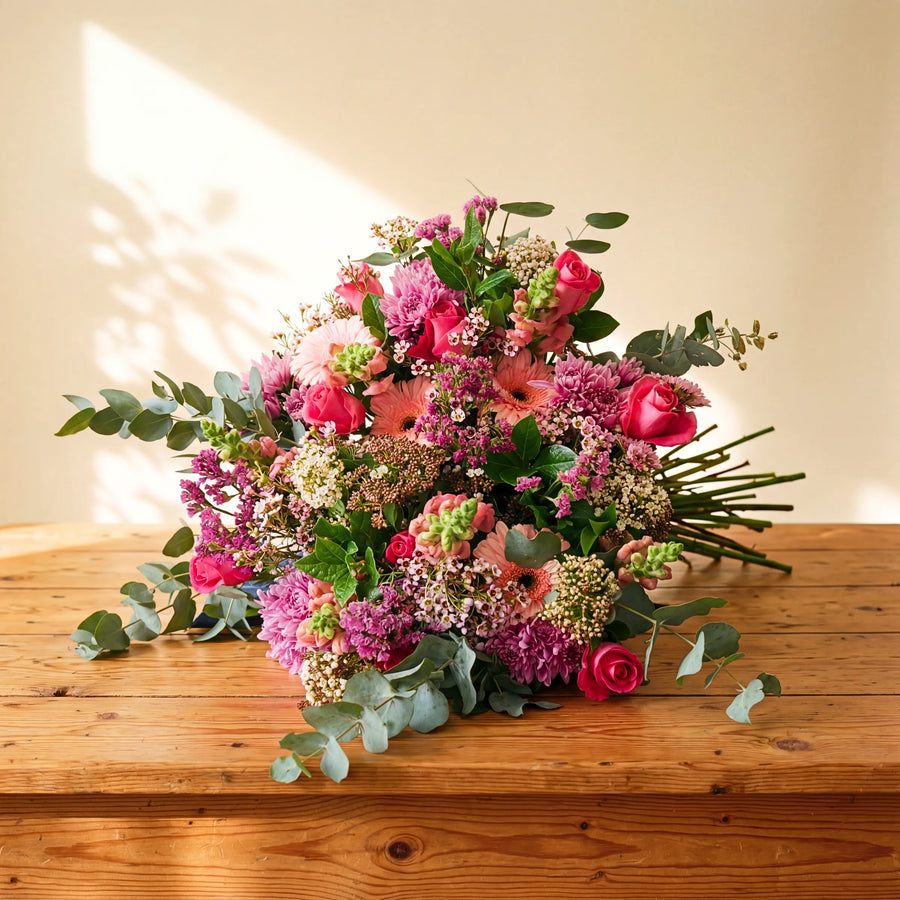 Country Garden Bouquet wild meadow hand-tied bouquet of pink roses, gerbera, chrysanthemums and eucalyptus on a wooden table