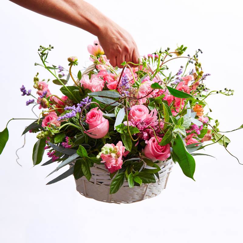 Bouquet of pink flowers in a white basket held by a hand on a white background