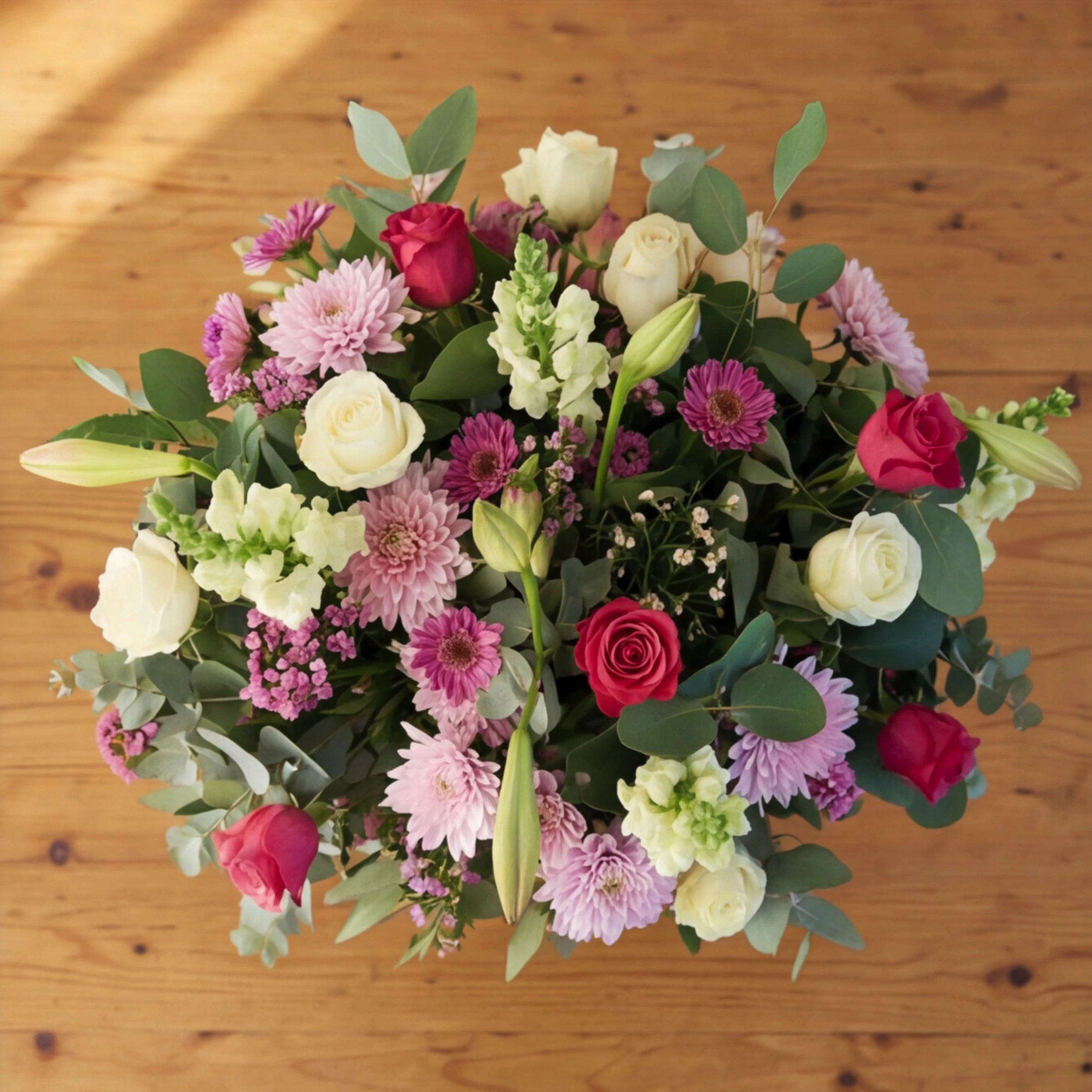 Overhead view of pink and white flowers, white and cerise roses, lilac chrysanthemums and gerberas with eucalyptus.