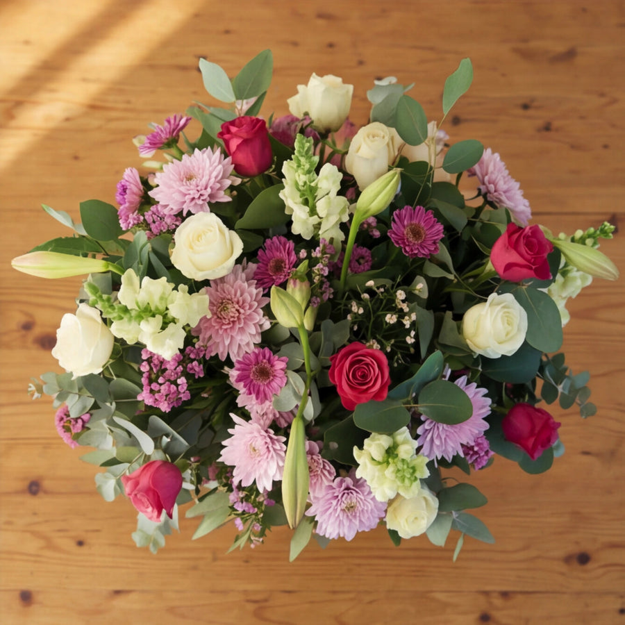 Overhead view of pink and white flowers, white and cerise roses, lilac chrysanthemums and gerberas with eucalyptus.