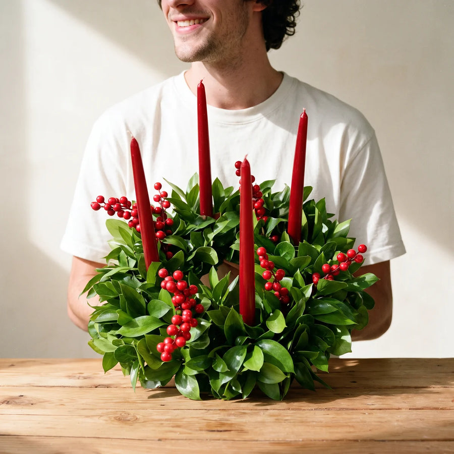 Man in a white t-shirt holding a green wreath with red candles and red berries, Fabulous Flowers South Africa