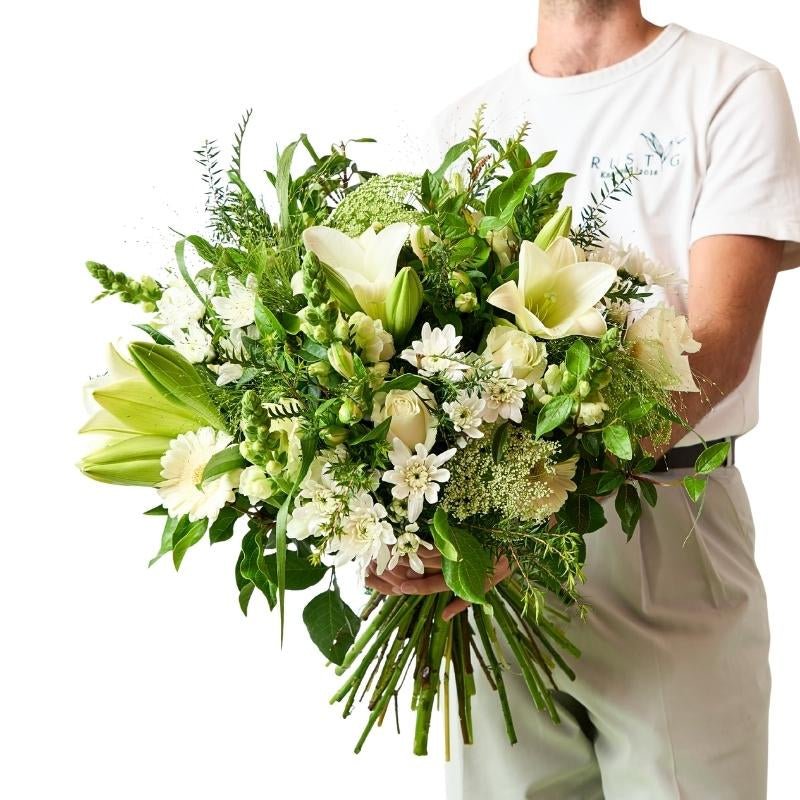 Person holding Elegant White Bouquet with lilies, white roses and lush greenery, wrapped for gifting