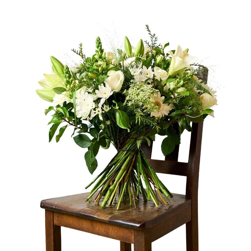 Elegant white bouquet arranged in vase on a wooden chair, featuring lilies, roses and greenery