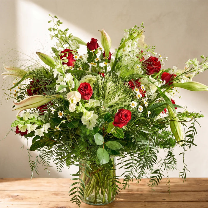 Large arrangement of red roses, white lilies, snapdragons and chamomile in a tall glass vase on a pine table, Fabulous Flowers South Africa