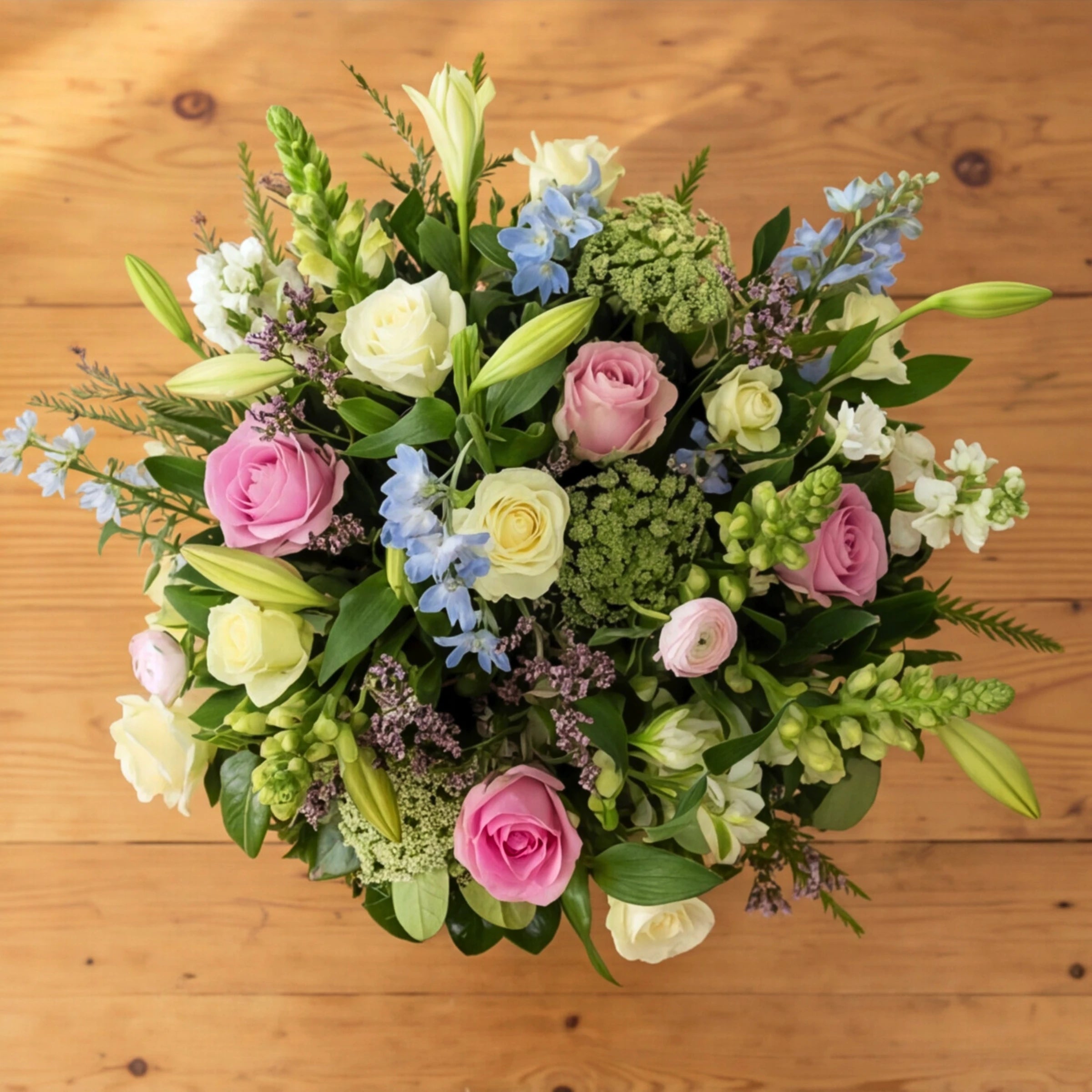 Top view of English Garden pastel arrangement showing pink and cream roses, blue delphiniums, snapdragons and Queen Anne's lace