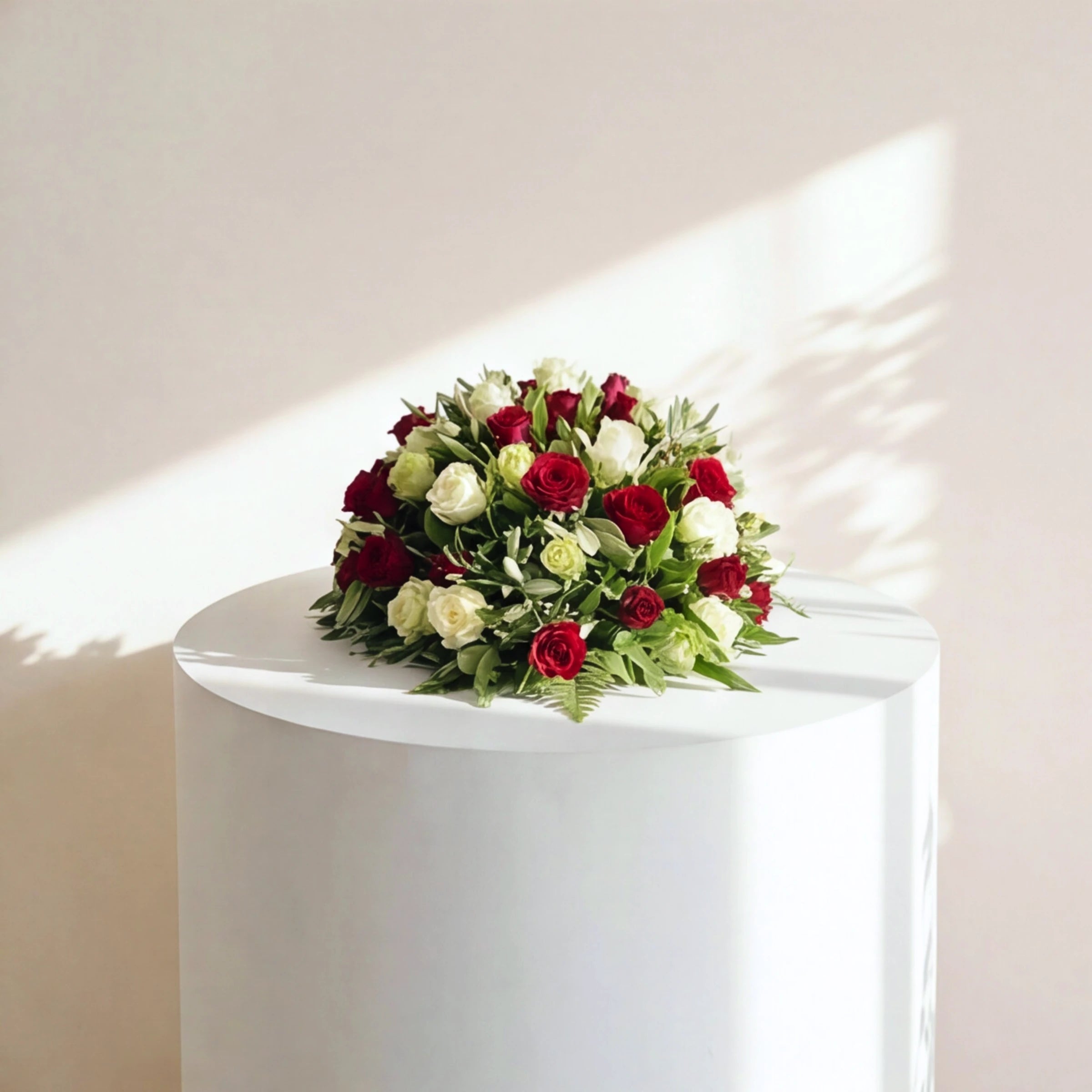 Front view of the Evermore casket spray with red and white roses resting among olive leaves