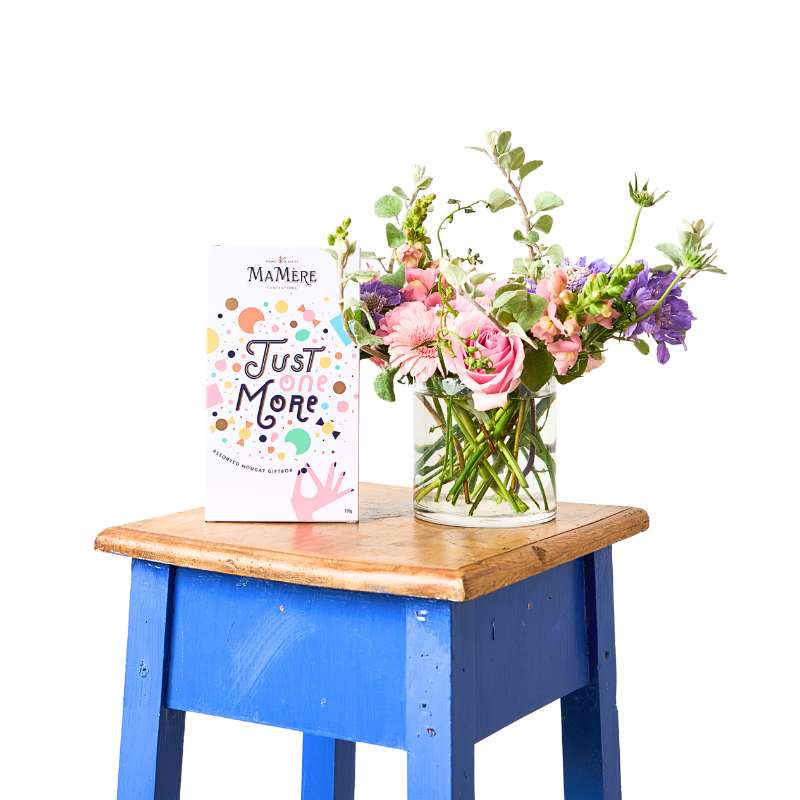 Blue stool with a wooden top holding a vase of flowers and a book titled 'Just One More'.