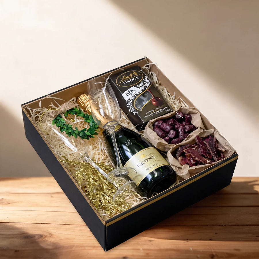 Open black gift box with sparkling wine, two champagne flutes, dark chocolate, biltong and droe wors on a pine table, Fabulous Flowers South Africa