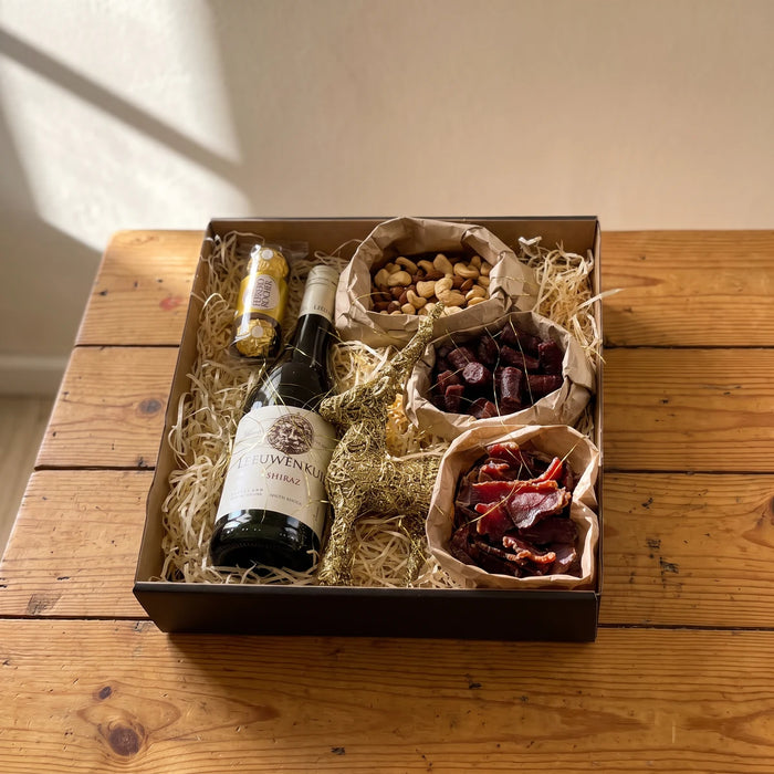 Open Christmas gift box with red wine, Ferrero Rocher, biltong, droewors and mixed nuts on a pine table, Fabulous Flowers South Africa