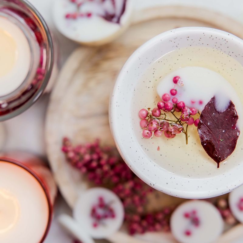 Close-up of a dessert with pink berries and a leaf, surrounded by candles and more desserts.