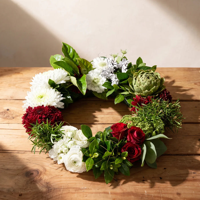 Fresh flower wreath of red roses, white and burgundy chrysanthemums, rosemary and an artichoke on a pine table, Fabulous Flowers South Africa