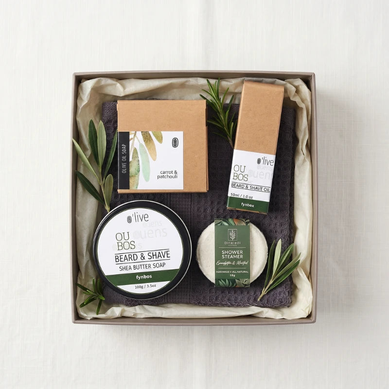 For Him Pamper Box flat-lay with Oubos Beard & Shave Oil, Shea Butter Shave Soap, Carrot & Patchouli Olive Oil Soap, Dinaledi Eucalyptus Shower Steamer and grey waffle hand towel styled with olive and rosemary sprigs, Fabulous Flowers and Gifts