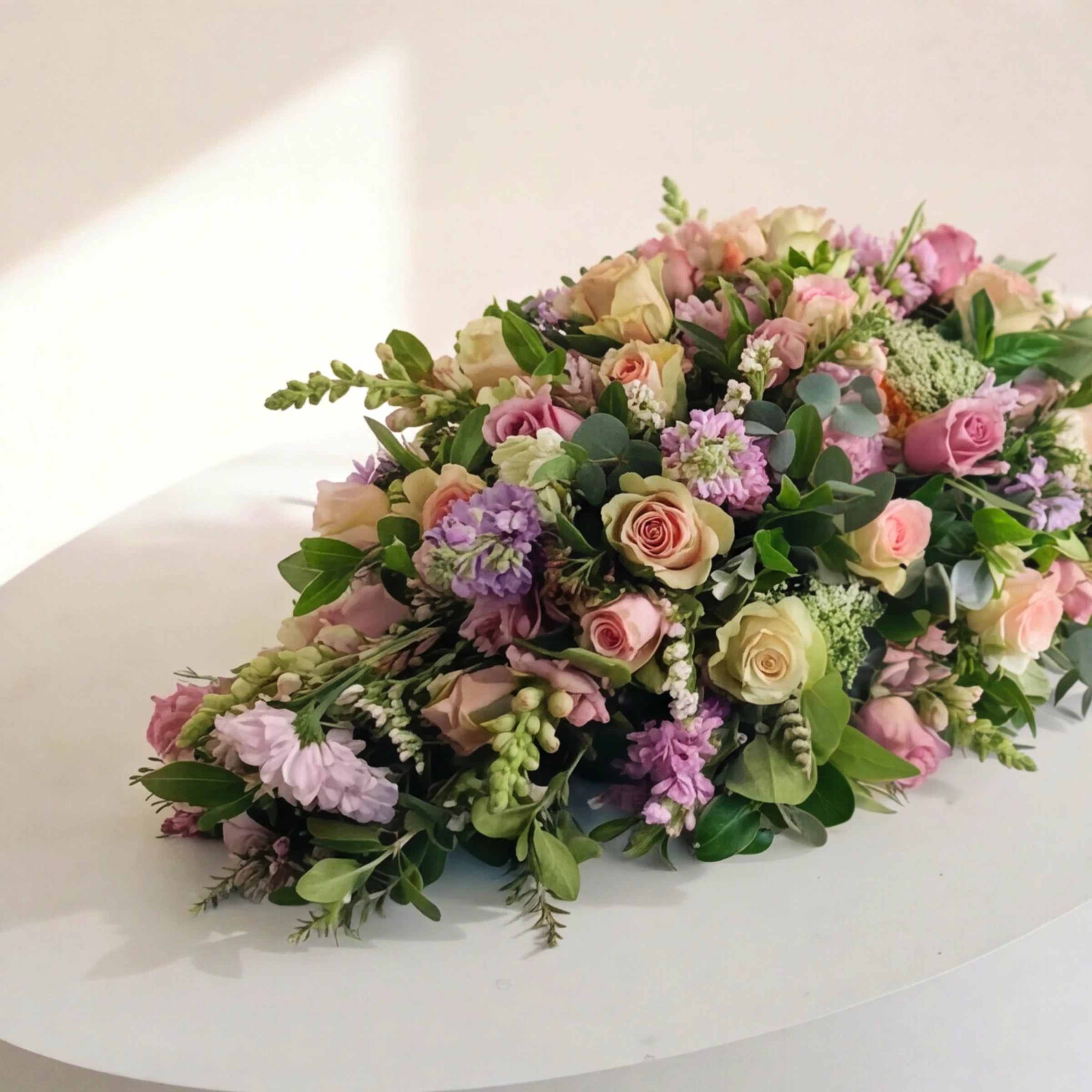 Side view of the Forever Loved coffin spray, pink and peach roses, lilac stocks and eucalyptus