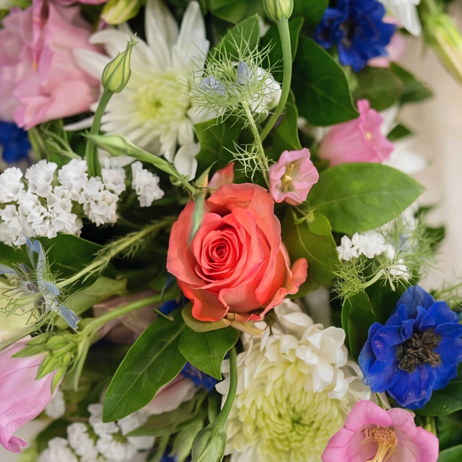 Detail of coral rose, white statice, blue delphinium and nigella in the Forget Me Not sympathy wreath