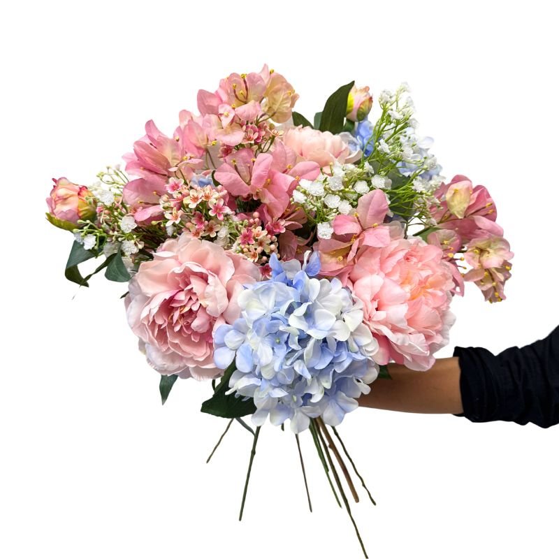 Bouquet of pink and blue flowers held by a hand on a white background