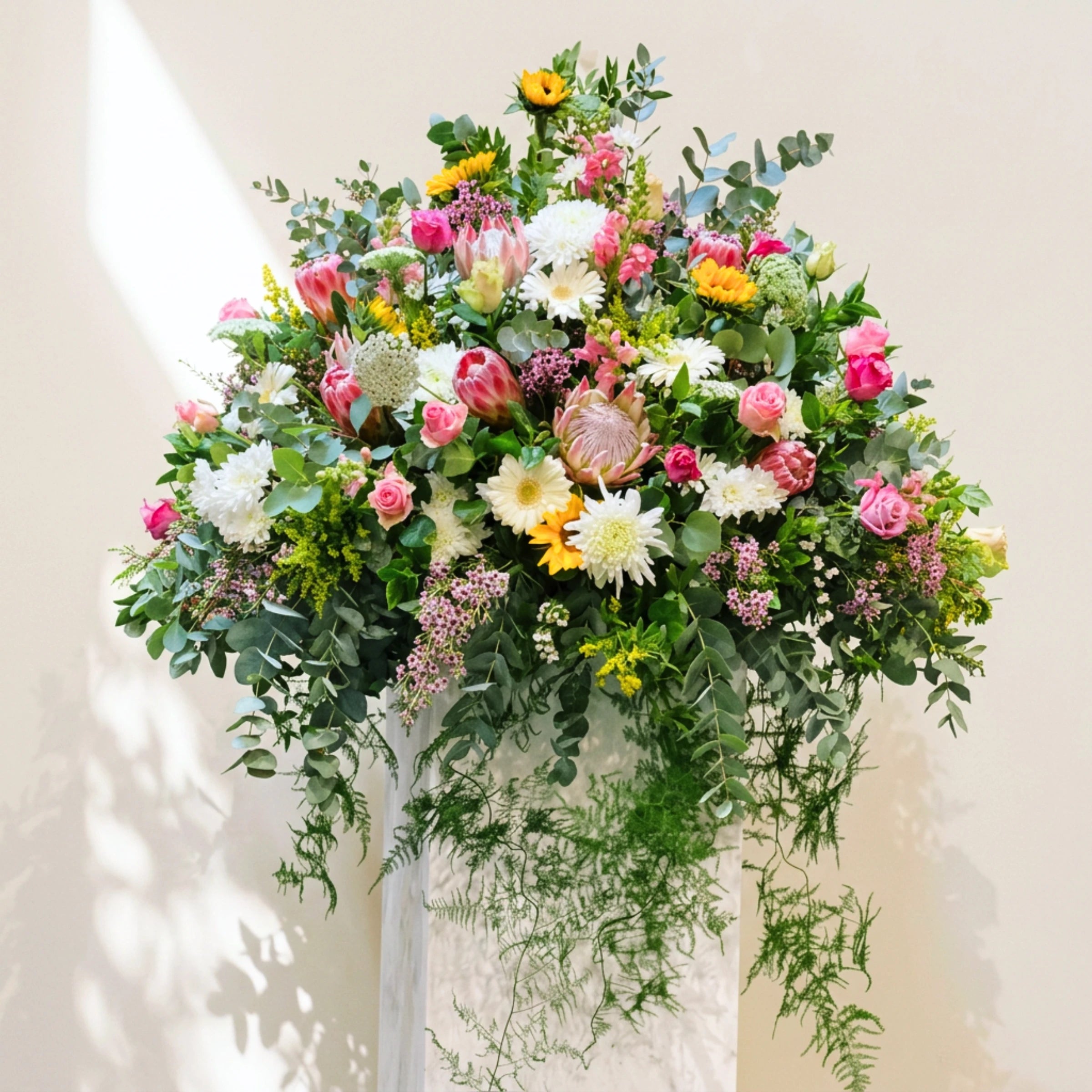Garden of Grace funeral service flowers, a large standing tribute of proteas, roses and gerberas on a plinth.
