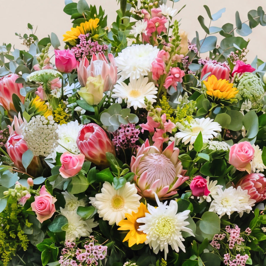 Pink proteas, white chrysanthemums, gerberas, pink roses and a sunflower in the standing funeral tribute.