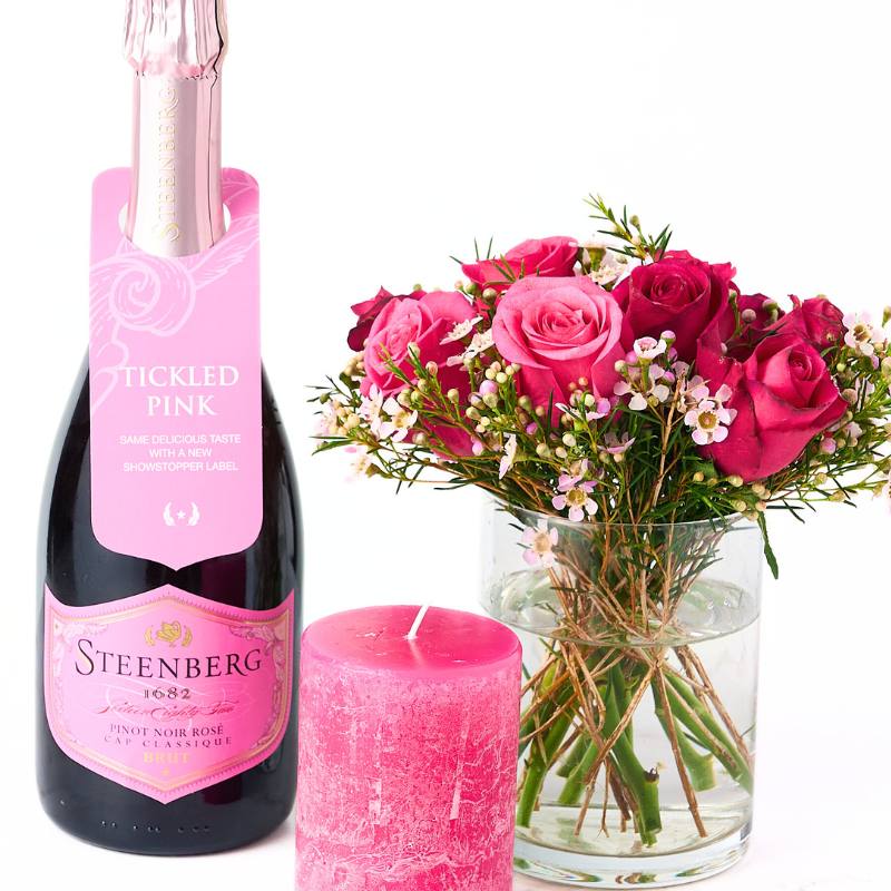 Steenberg Tickled Pink wine bottle with pink candle and bouquet of pink roses on a white background