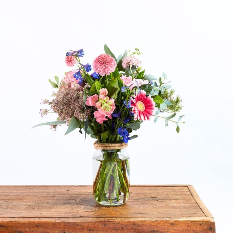 Arrangement of flowers in a clear vase on a wooden table with a white background