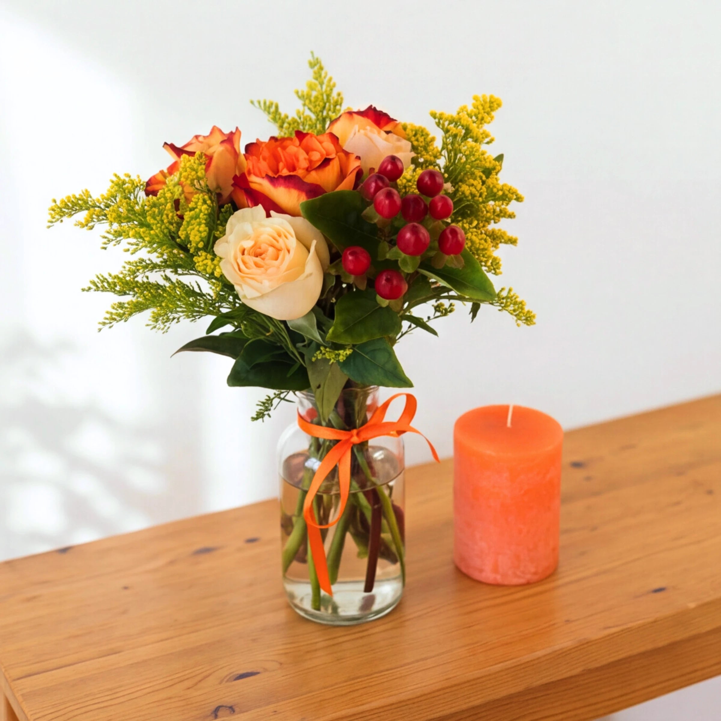 Golden Hour gift set with flowers in a vase and a burnt orange pillar candle on a wooden table
