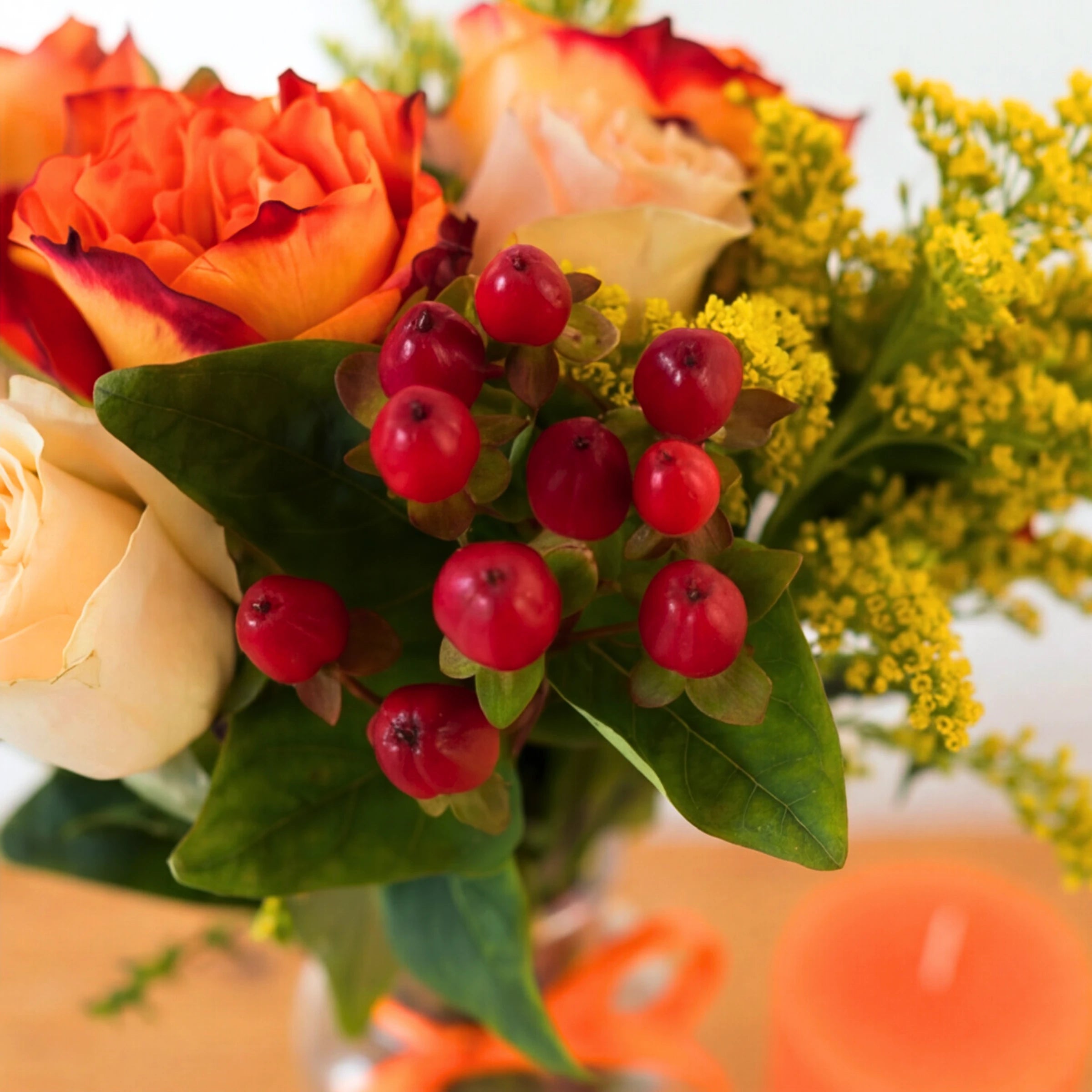 Close up of red hypericum berries, orange and cream roses and golden solidago in the Golden Hour posy