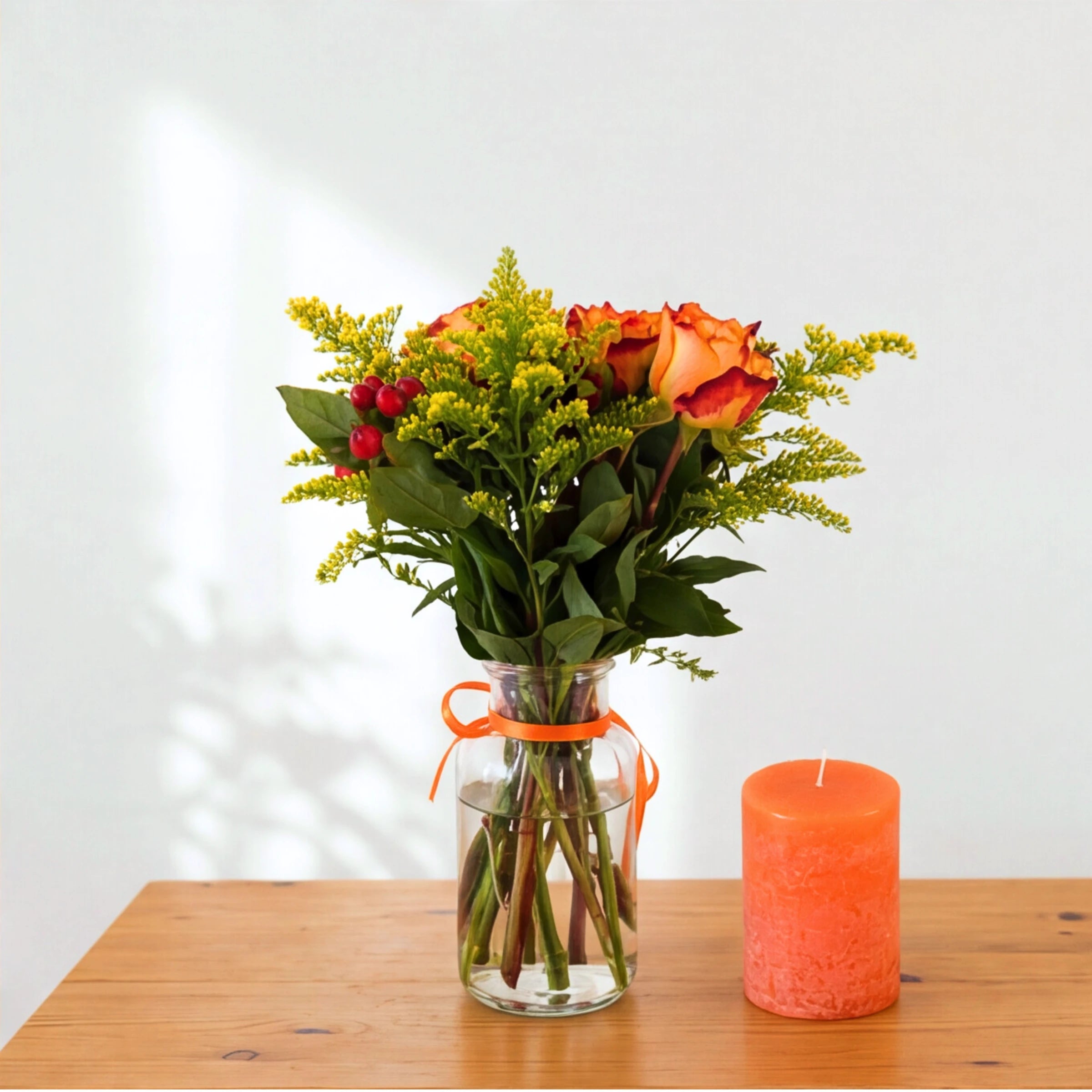Golden Hour set from behind showing greenery and solidago in a glass vase beside an orange candle