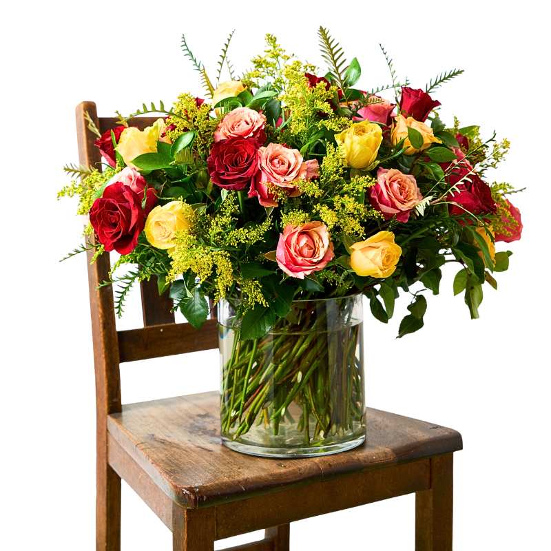 Arrangement of colourful flowers in a clear vase on a wooden chair with a white background