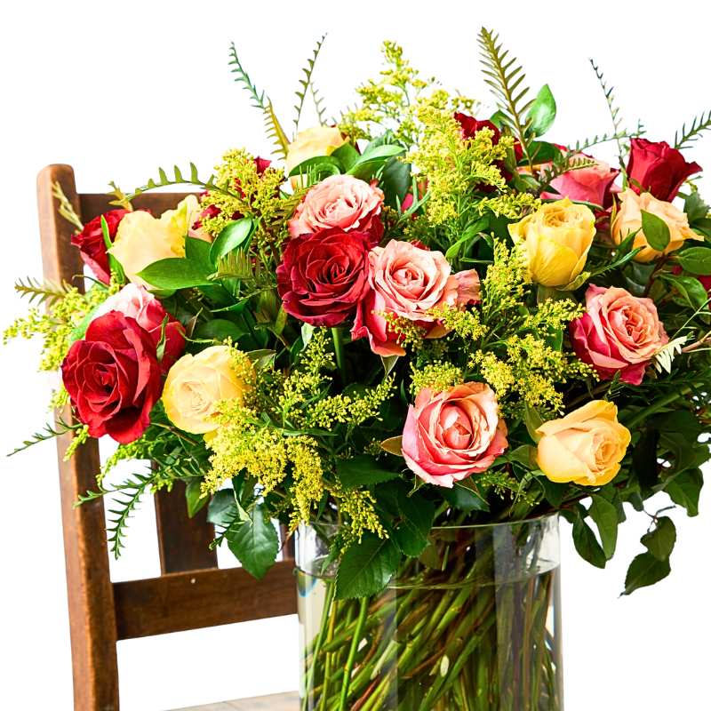 Arrangement of colourful flowers in a clear vase on a wooden chair.