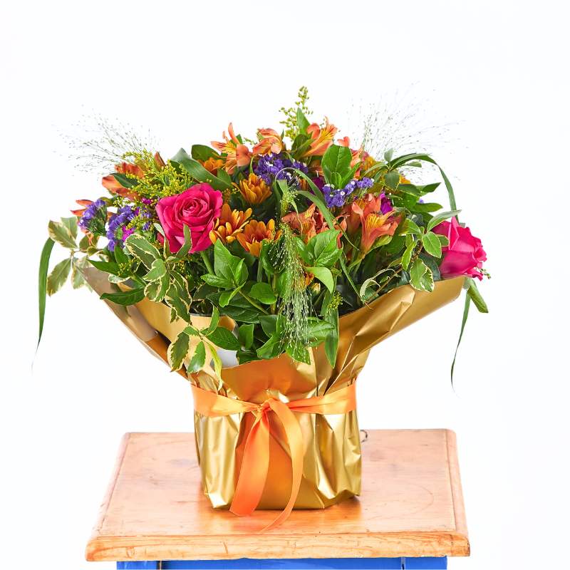 Arrangement of flowers wrapped in gold paper on a wooden table with a white background