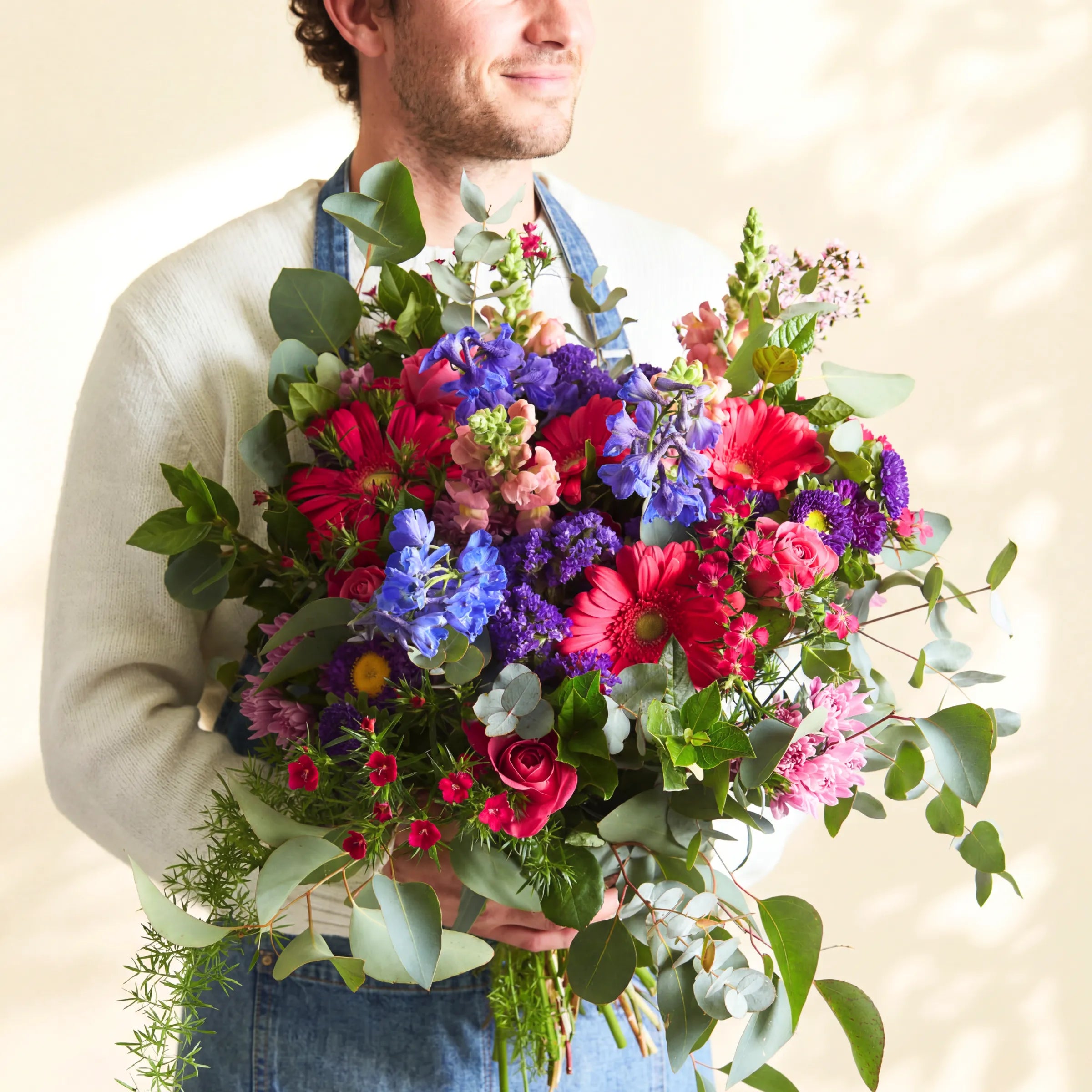 Fabulous Flowers florist holding the Gratitude thank you bouquet of cerise gerberas, blue delphinium and eucalyptus
