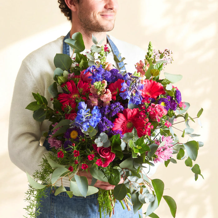 Fabulous Flowers florist holding the Gratitude thank you bouquet of cerise gerberas, blue delphinium and eucalyptus