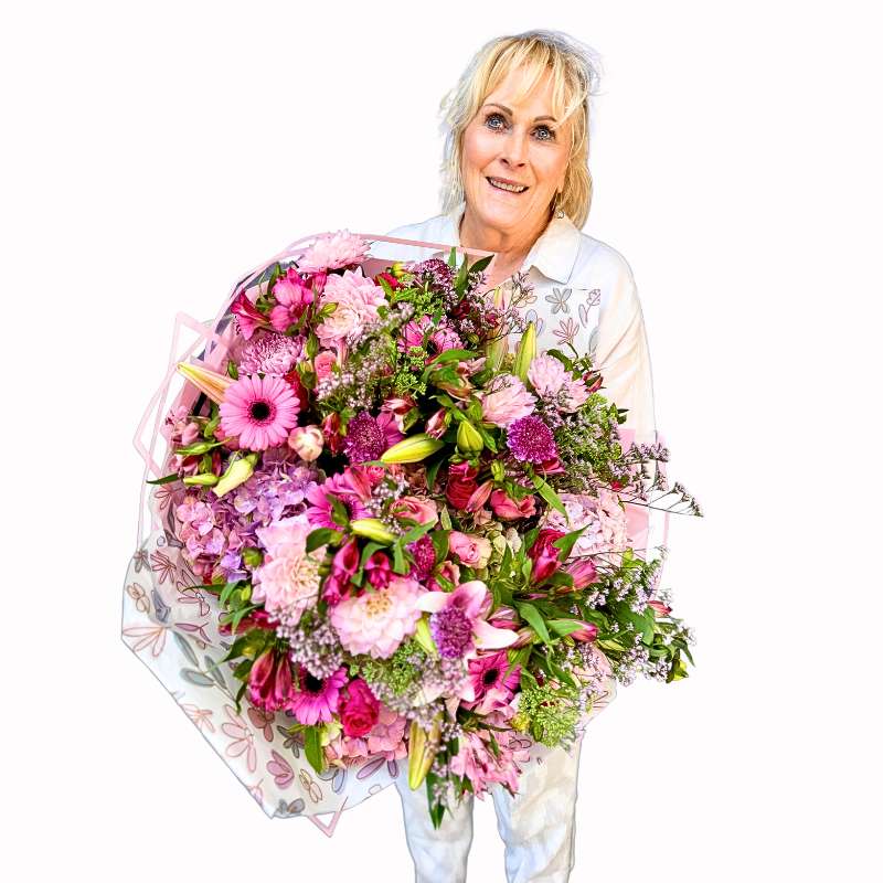 Handle with Love Bouquet held by a woman, featuring pink gerbera daisies, garden roses, lilies and berry-toned seasonal blooms