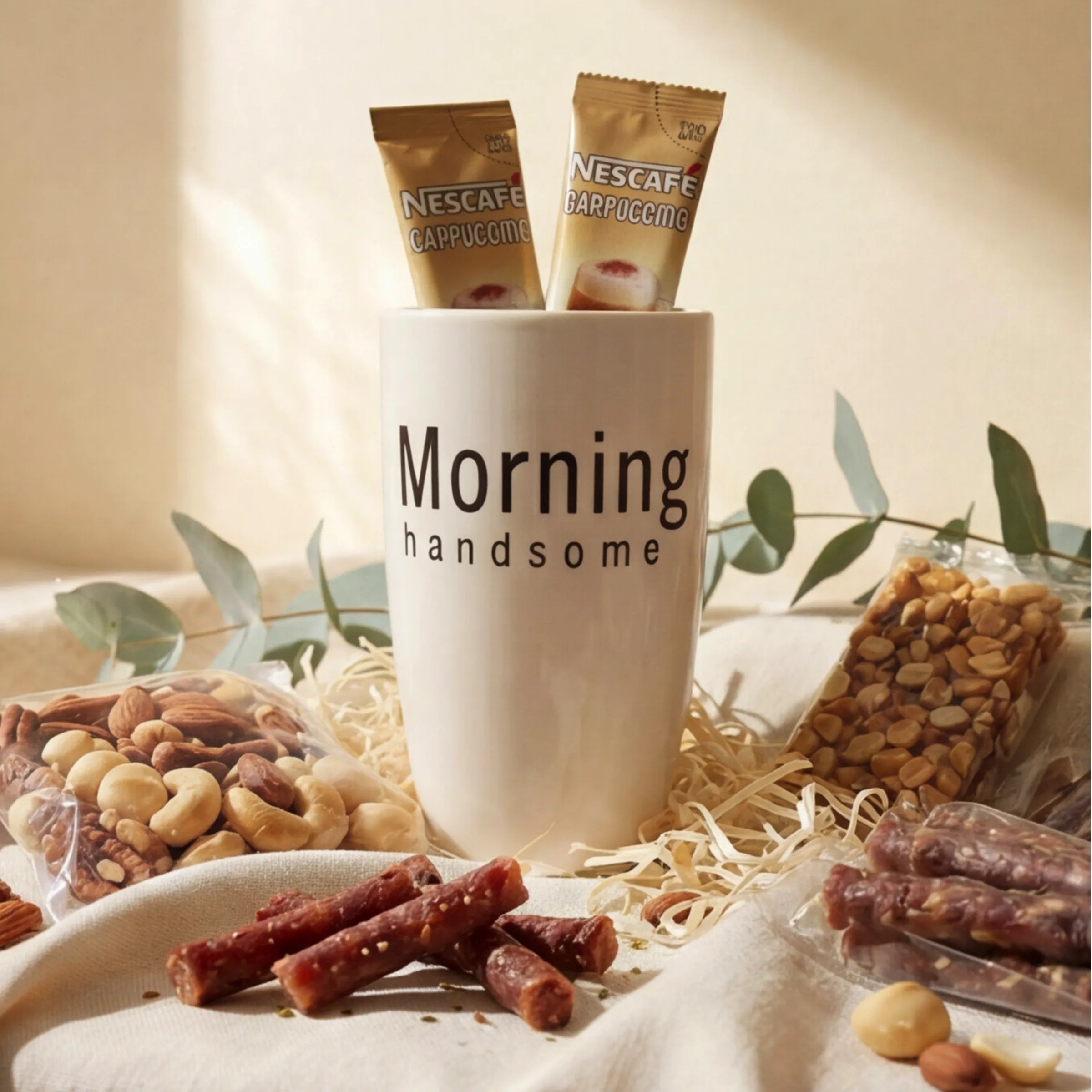 Close-up of Hello Handsome Hamper showing the Morning Handsome mug filled with Nescafé Cappuccino sachets, a bag of mixed nuts, a peanut nougat bar and South African droëwors sticks styled with eucalyptus on linen, hand-packed by Fabulous Flowers South Africa