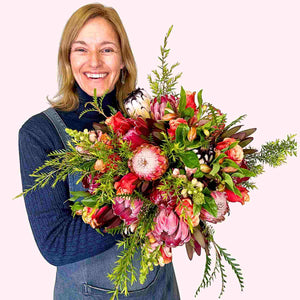 Joyful Jayne presenting her vibrant bouquet with red and pink flowers including proteas, named Jayne's Flower Bouquet from Fabulous Flowers and Gifts.