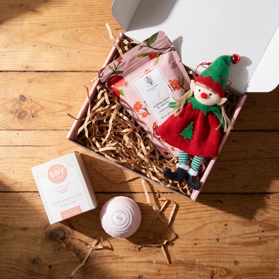 Pink gift box of bath salts and a felt elf ornament seen from above, with a soy candle box and a pink bath bomb beside it on a wooden table, Fabulous Flowers South Africa