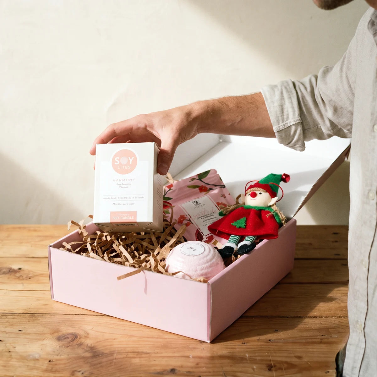 Man lifting a soy candle box out of a pink gift box with bath salts, a bath bomb and an elf ornament, Fabulous Flowers South Africa
