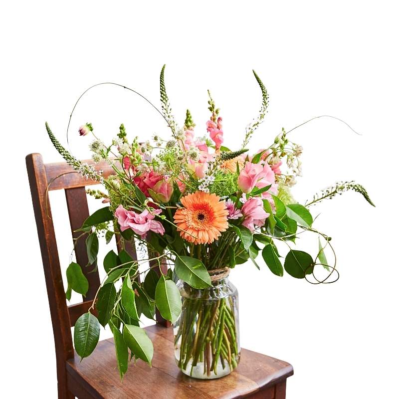 Joy in a Large Jar arrangement with pastel blooms and fresh greenery in a clear glass jar on a wooden chair