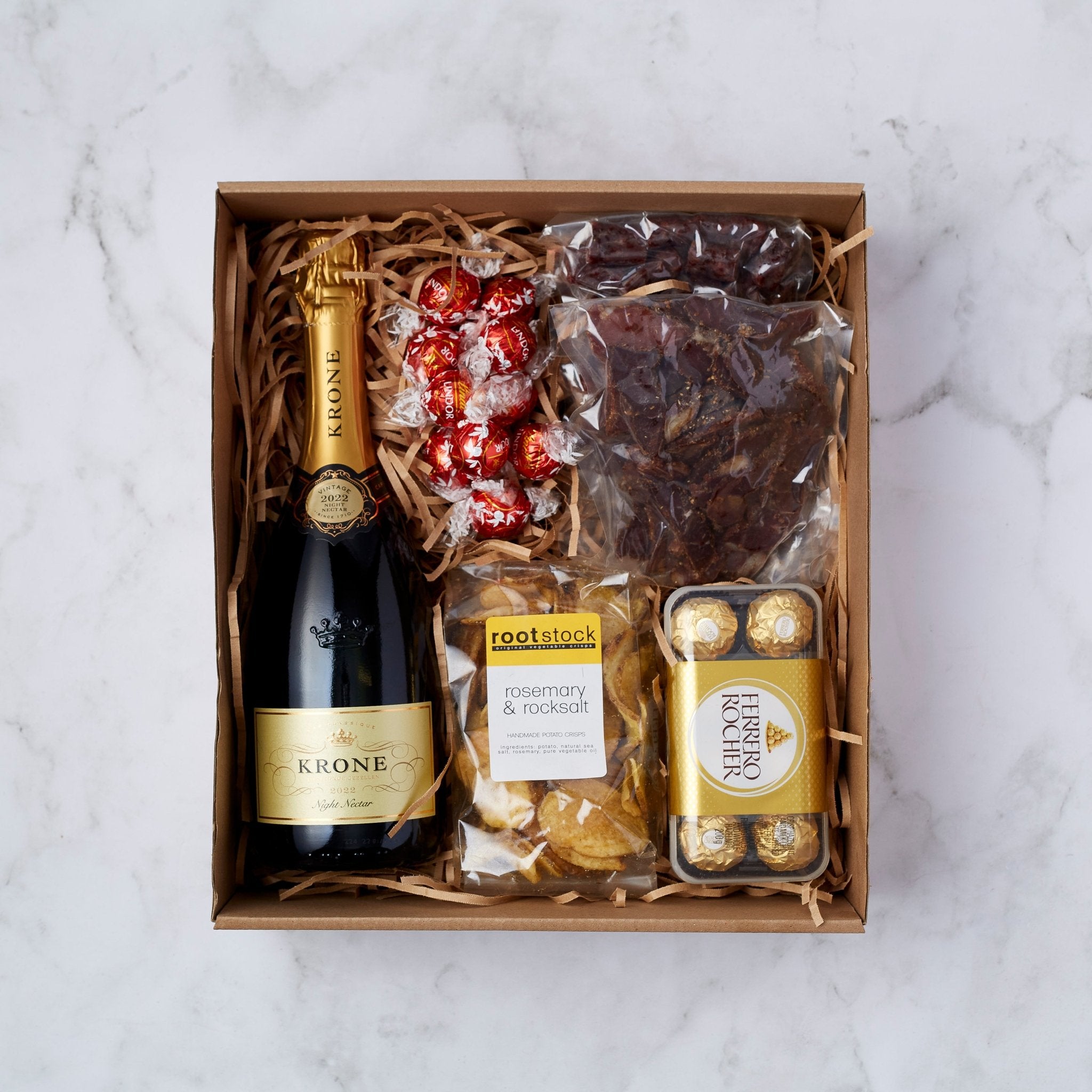 Gift box with Krone sparkling wine, Lindor truffles, biltong, rosemary & rock salt crisps, and Ferrero Rocher chocolates.