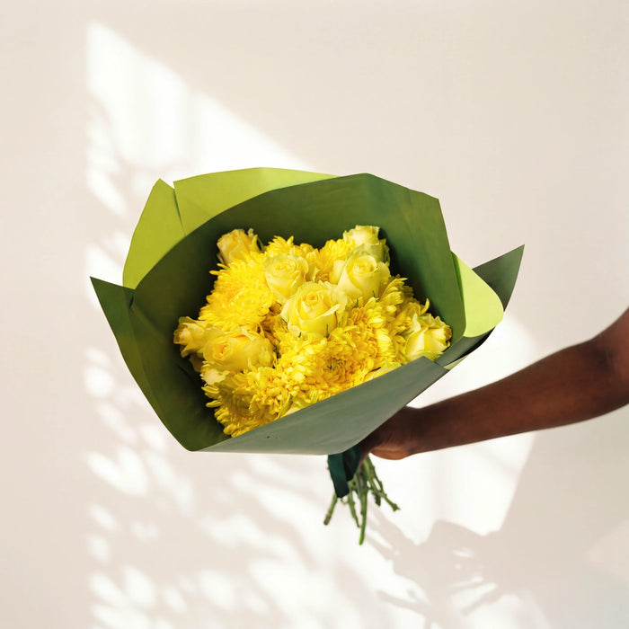 Limoncello yellow roses bouquet held against a sunlit wall, yellow roses and chrysanthemums in green wrap