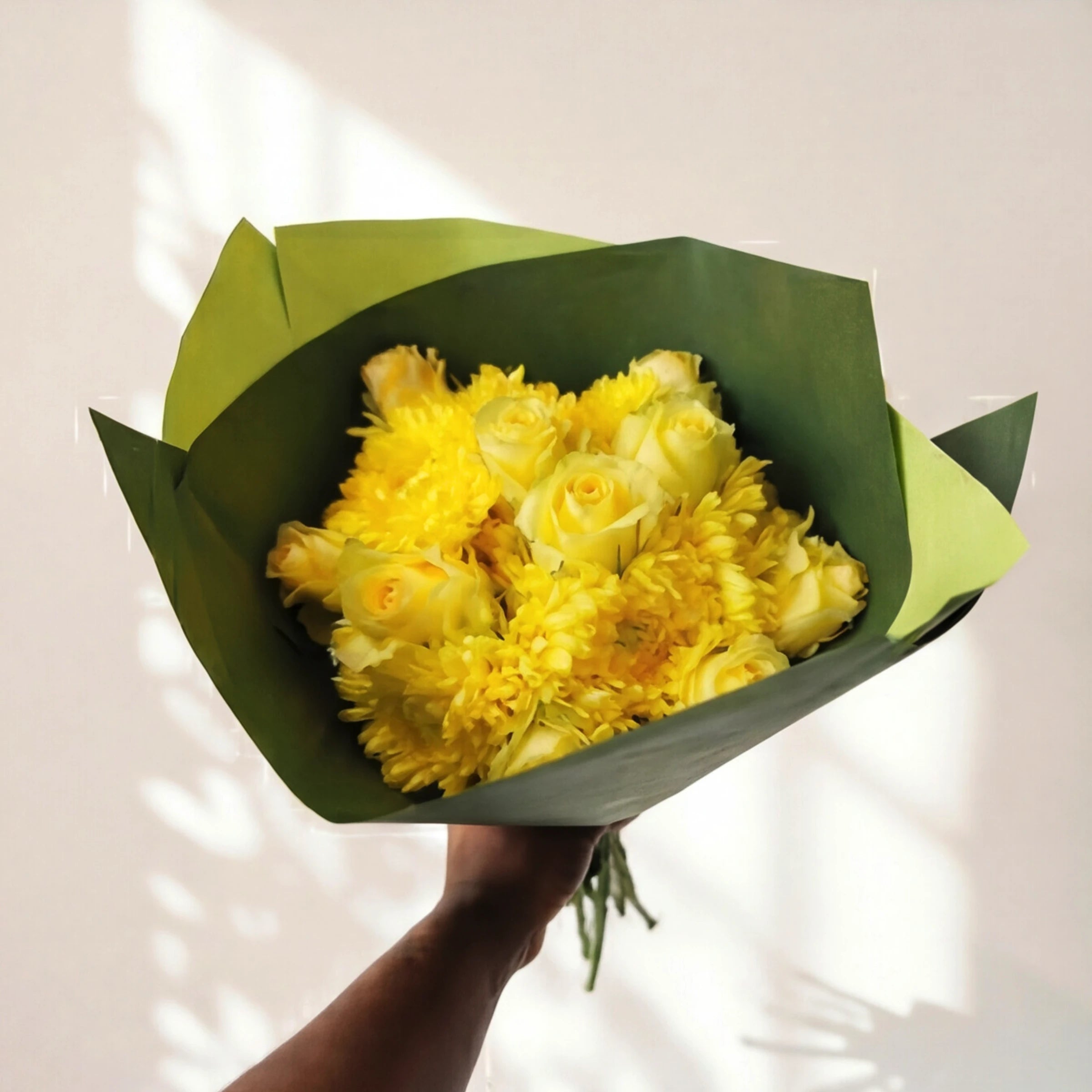 A hand holding up the full Limoncello bouquet, yellow roses and yellow chrysanthemums wrapped in green