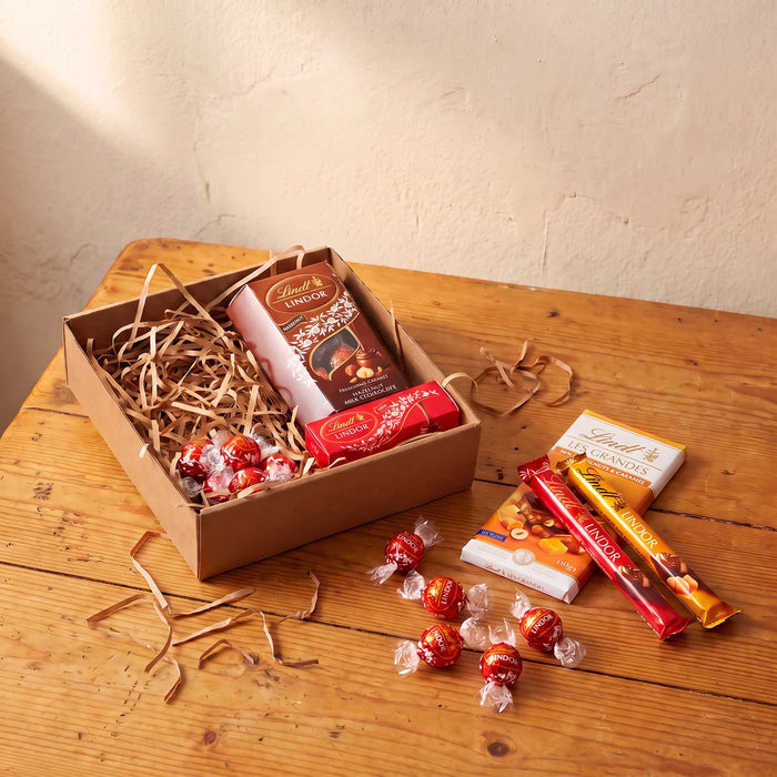 Kraft gift box with a Lindor Hazelnut cornet and truffles, beside a Les Grandes bar, two Lindor sticks and loose Lindor truffles on a pine table, Fabulous Flowers South Africa