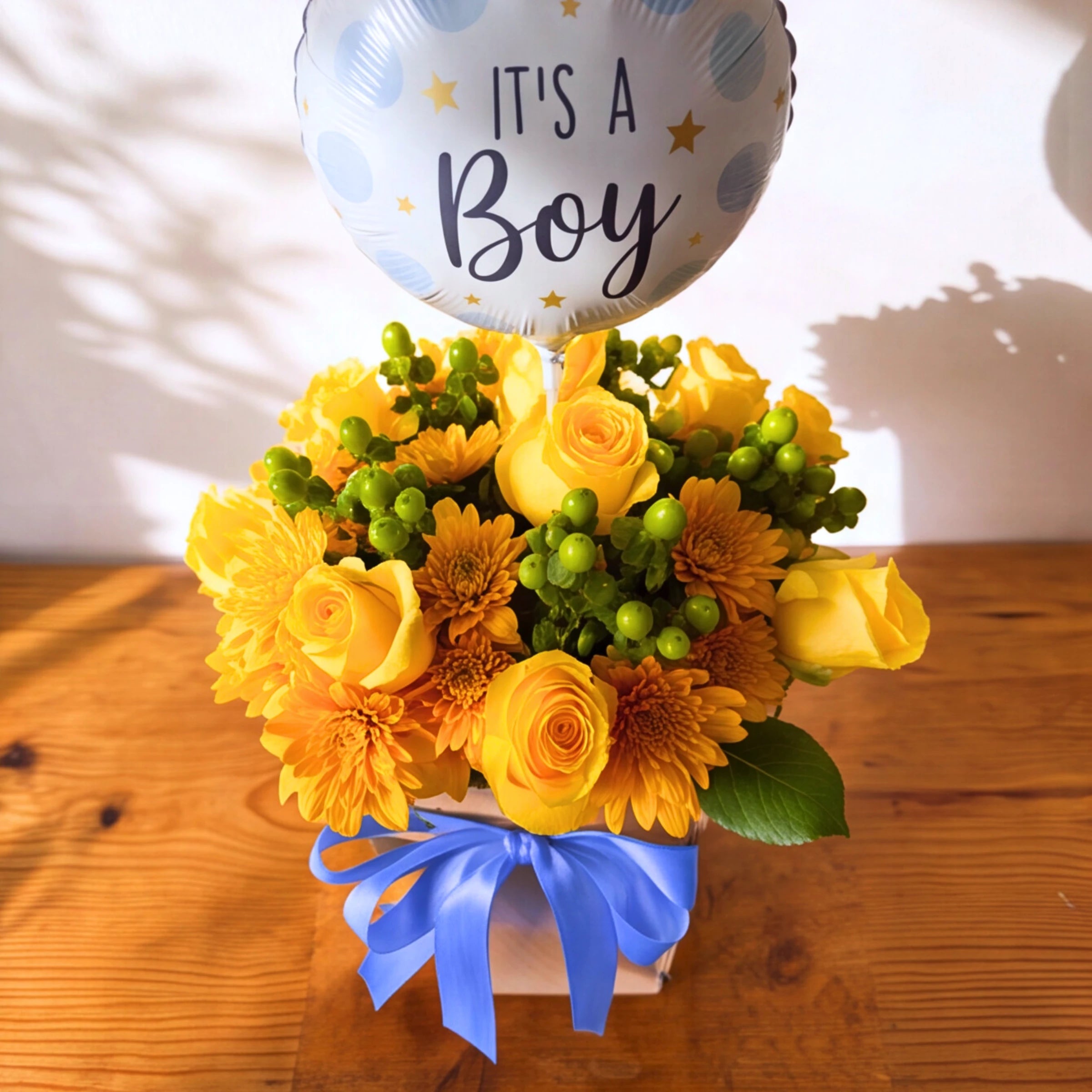 Little Prince baby boy flower box with blue satin bow and It's a Boy foil balloon on a wooden table