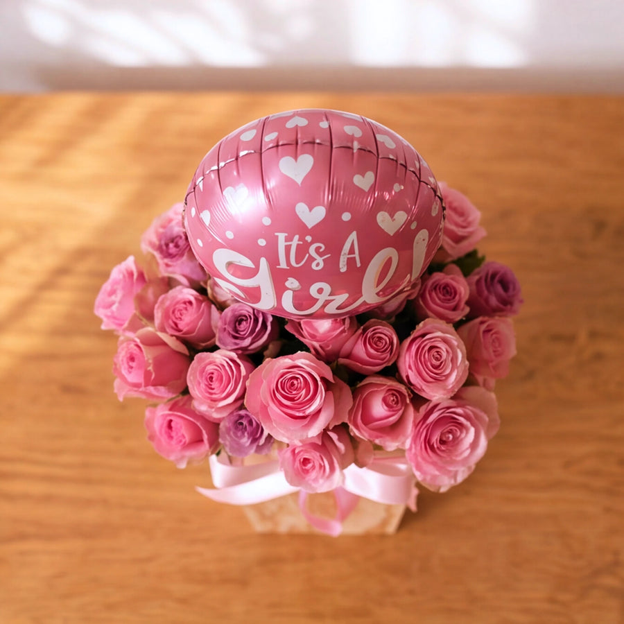 Overhead view of pink and lilac roses with an It's a Girl balloon in the Little Sweetheart baby girl box