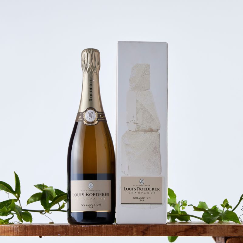 Elegant Louis Roederer Champagne is displayed on a wooden surface with leafy green accents against a light backdrop.
