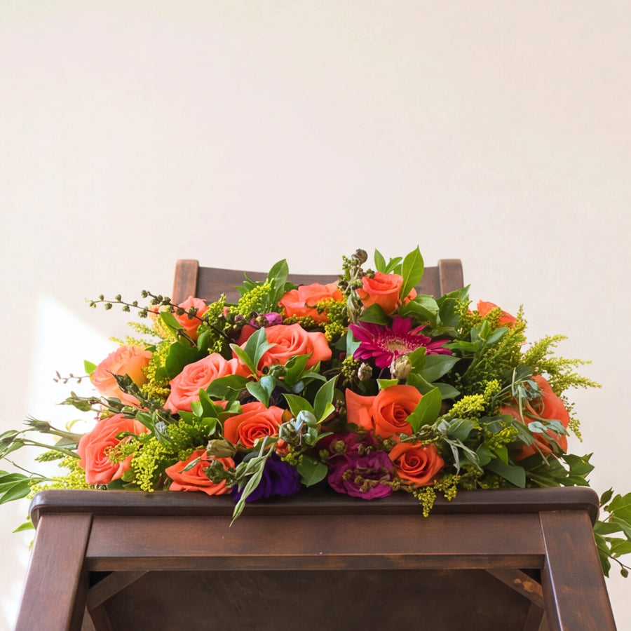 The Lush and Lovely orange and pink bouquet with solidago and greenery on a wooden chair