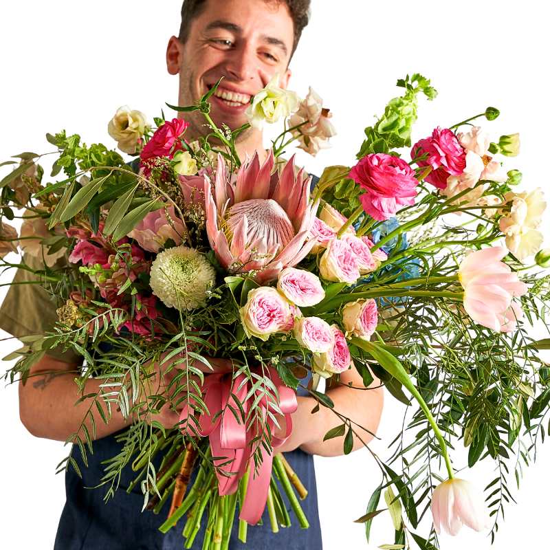 Man holding an oversized luxury florist choice bouquet with exotic mixed blooms and trailing greenery